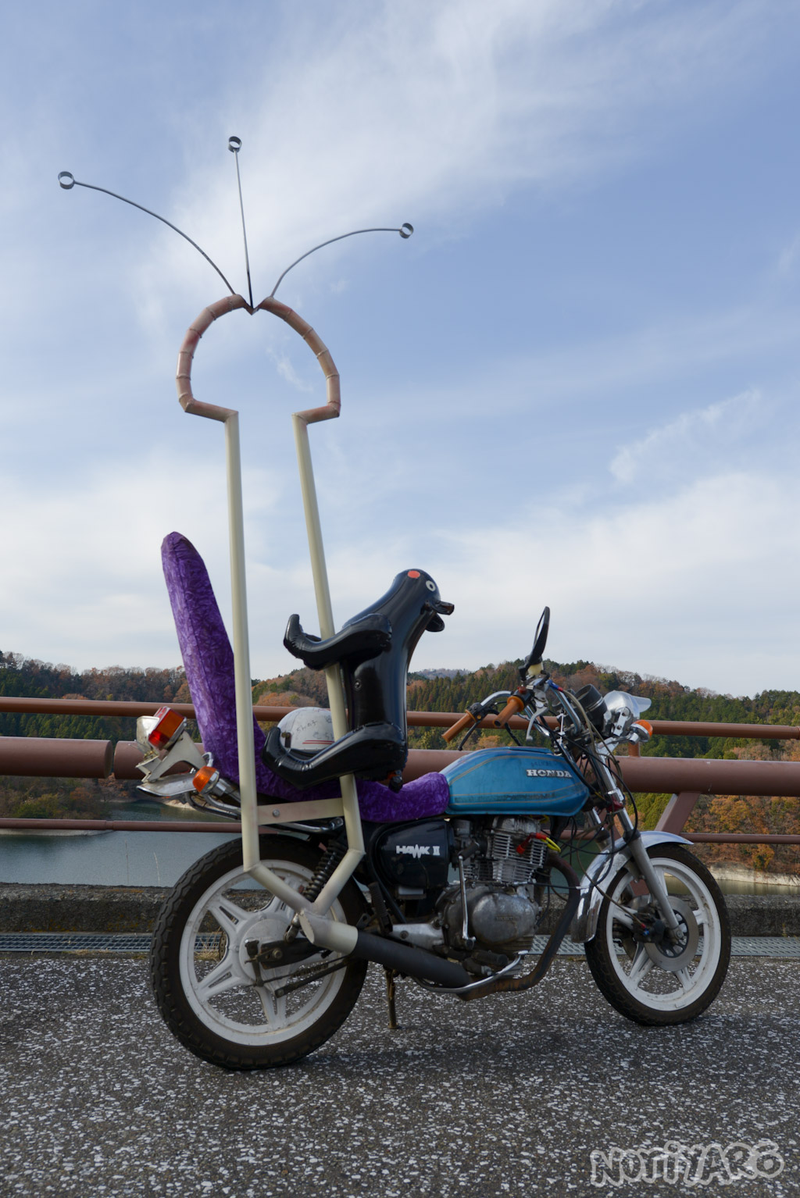 A Phallic shaped exhaust on a bike, mid ejaculation with a black cat